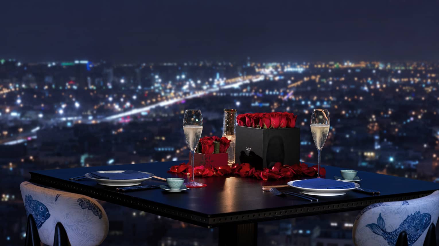 Sintoho dining table, red roses and Champagne glasses by window overlooking city lights below