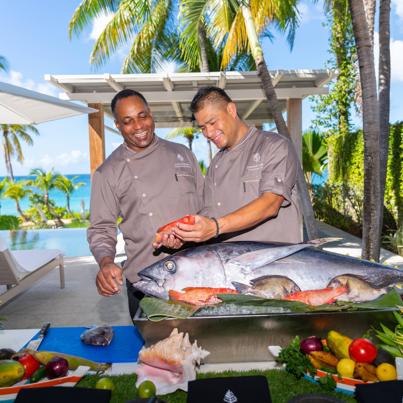 Two people standing in front of a food display with a large fish while holding a smaller fish.