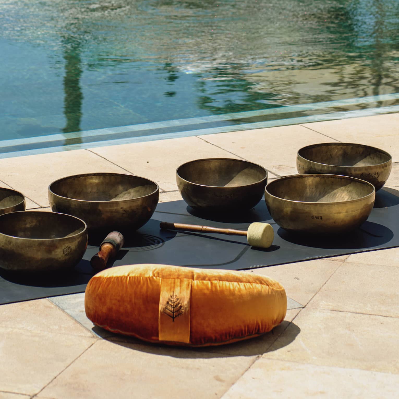 Sound healing bowls in front of a pool and white lounge chairs with umbrellas