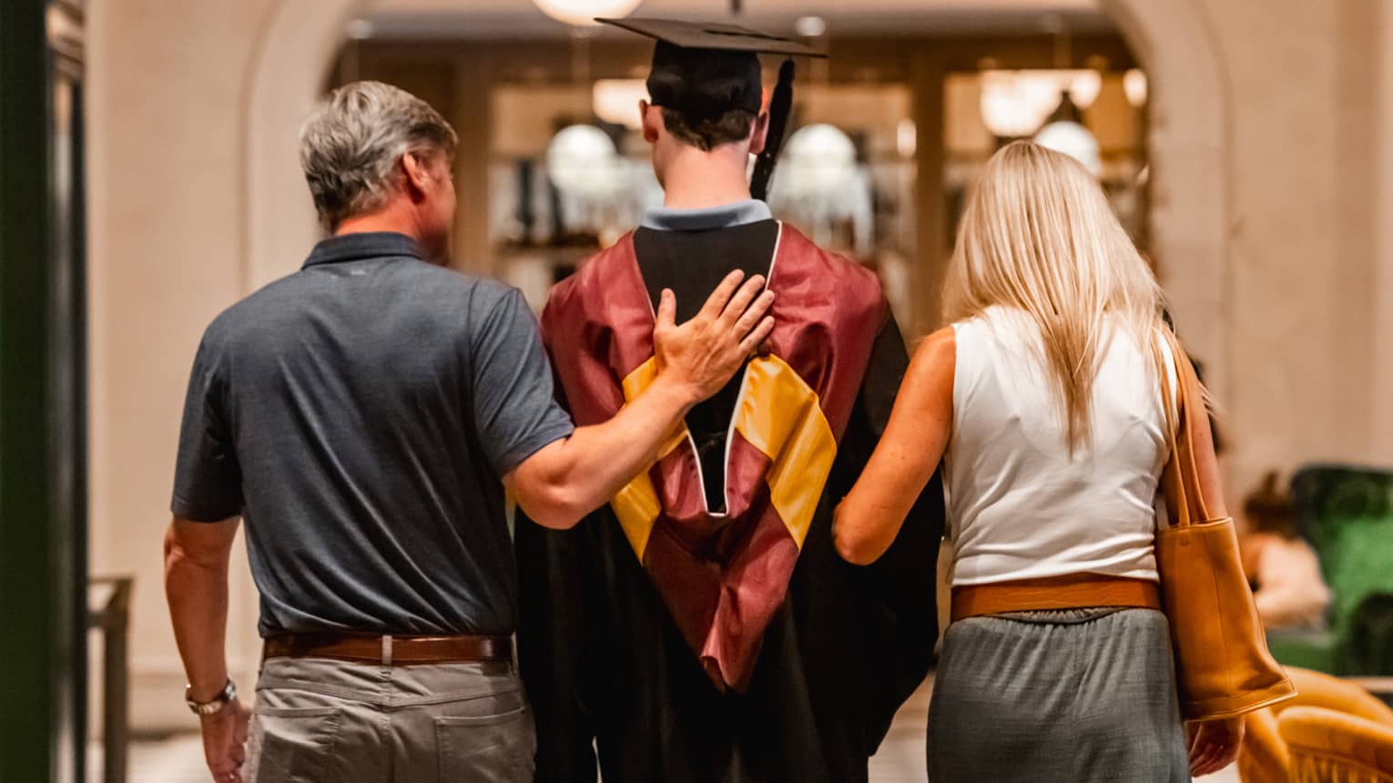 Parents walking with child in graduation gown.
