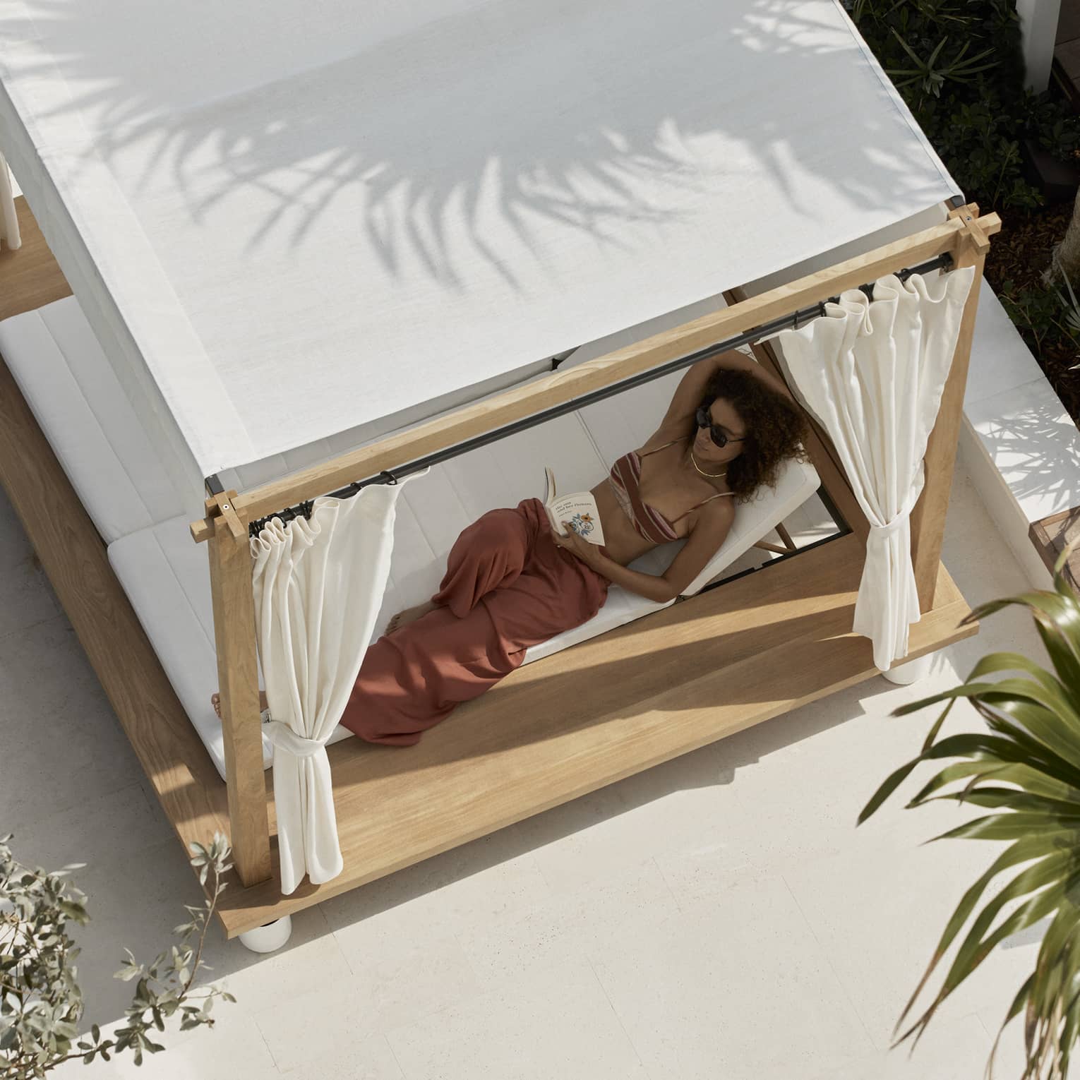 Aerial view of woman lounging in a covered poolside daybed