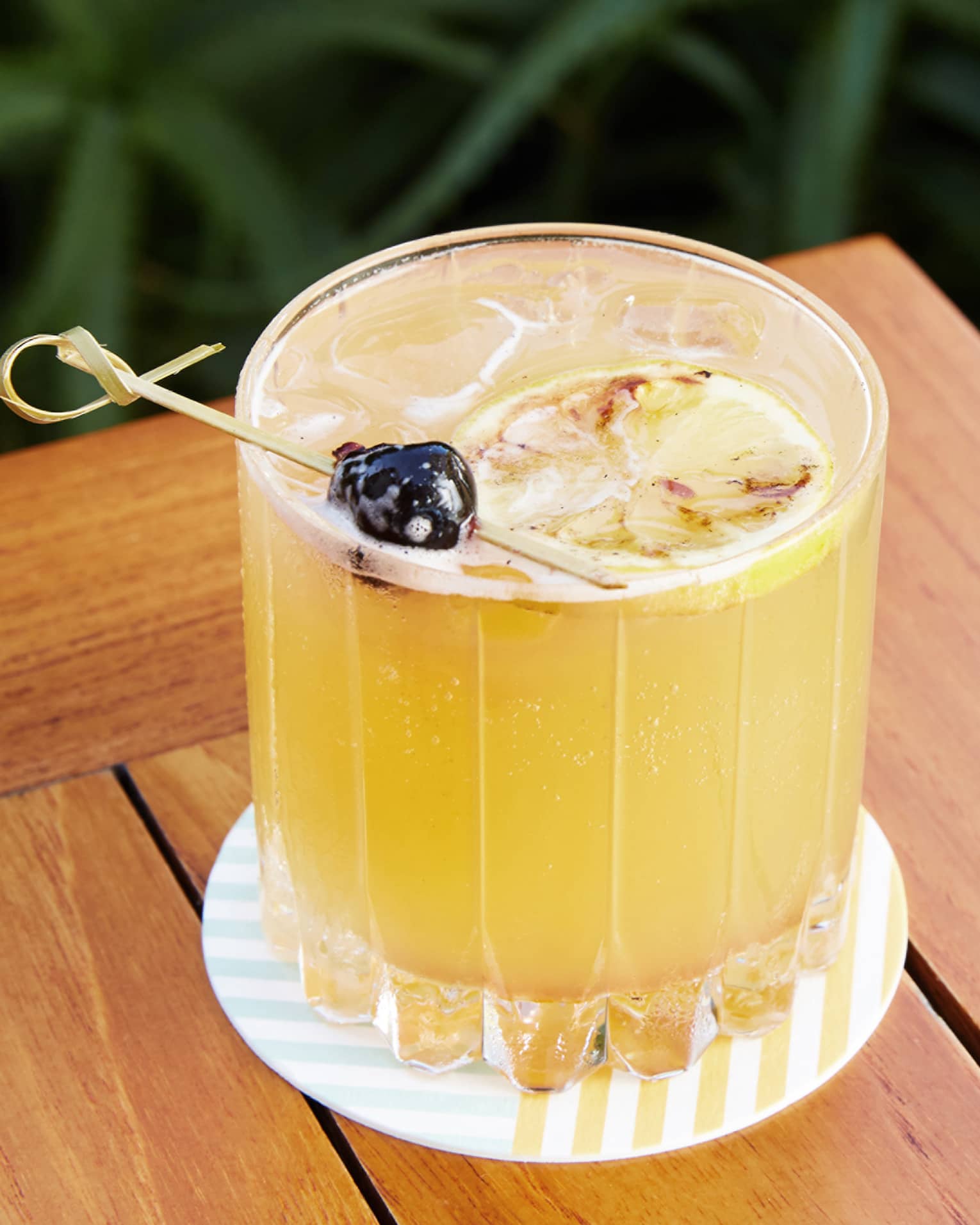 Yellow drink in a glass on a coaster on an outdoor table.