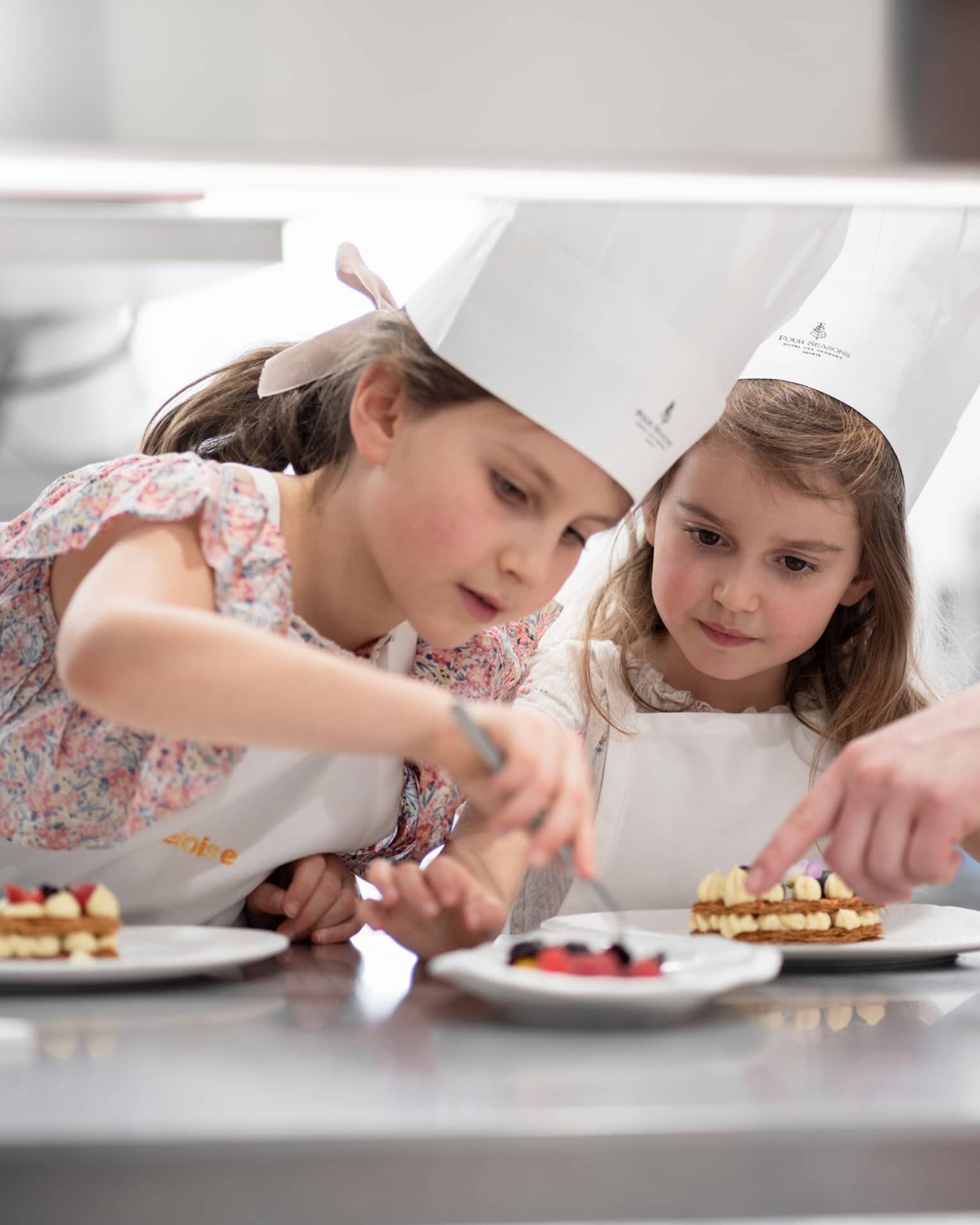 Two children in chef hats carefully decorating plates of desserts during a pastry-making class