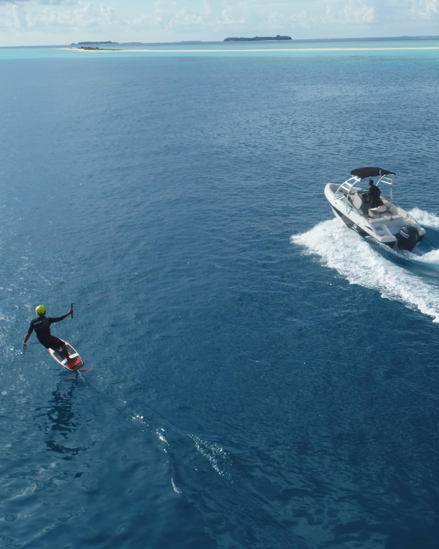 An aerial view of someone wakeboarding behind a small speed boat