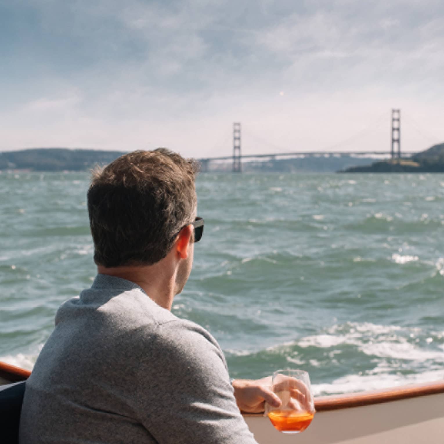 A man enjoys a drink as he relaxes on a boat, the Golden Gate Bridge in the distance