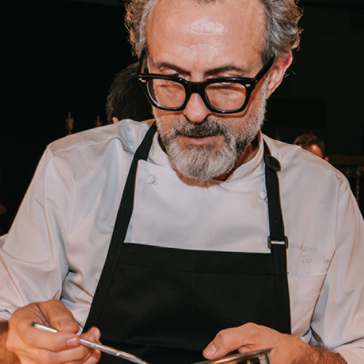Person wearing a chef’s coat and apron and stirring food in a bowl