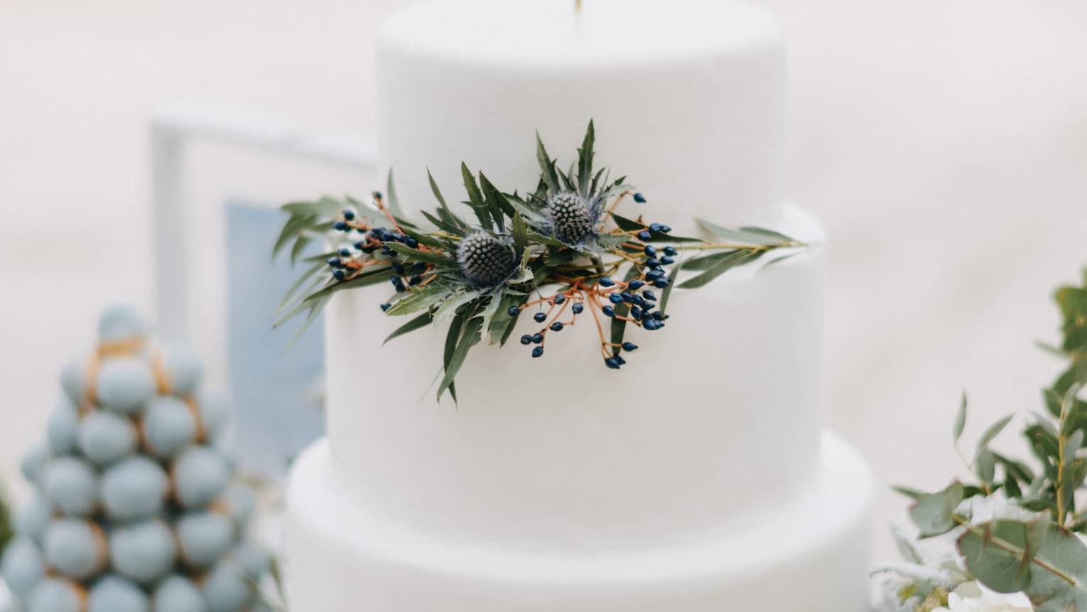 Three tiered wedding cake decorated with green leaves, white flowers