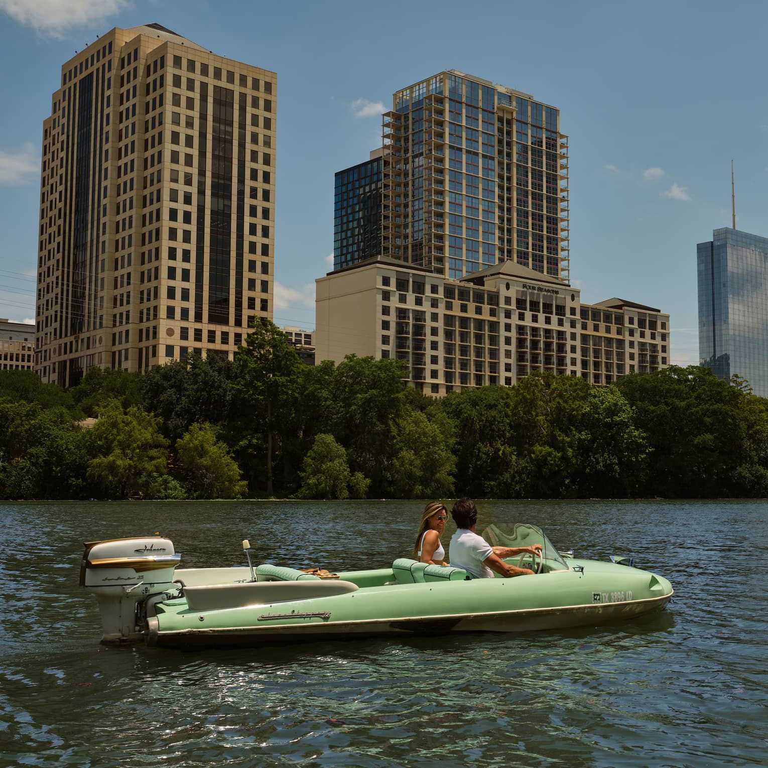 Two guests on a boat in the water with city buildings in the background