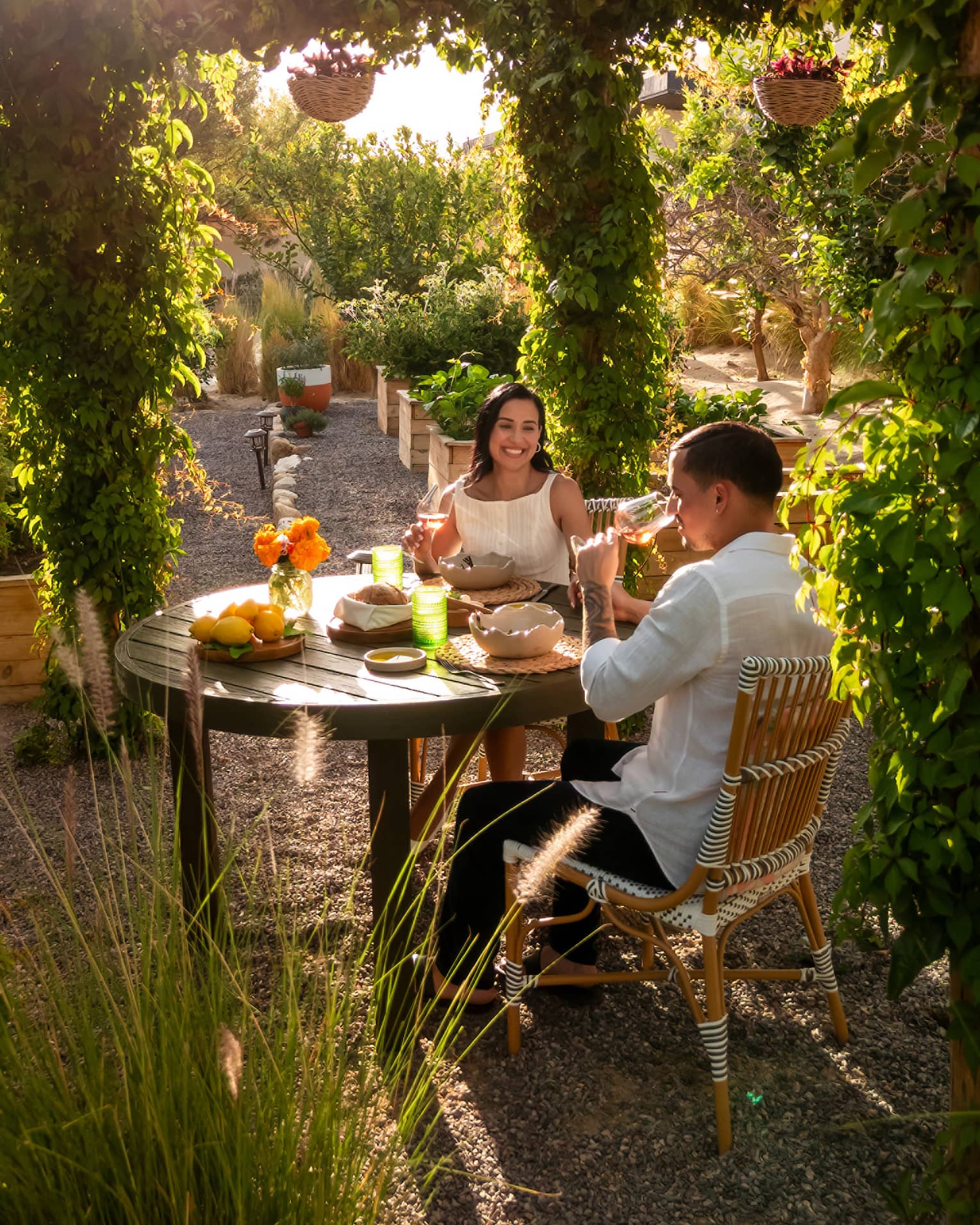 Two people at a small outdoor dining table in an outdoor space surrounded by lush greenery