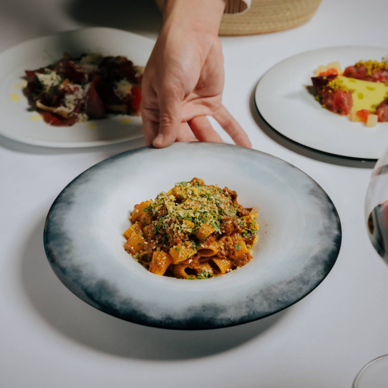 Hand places a bowl of pasta onto a white-linen table