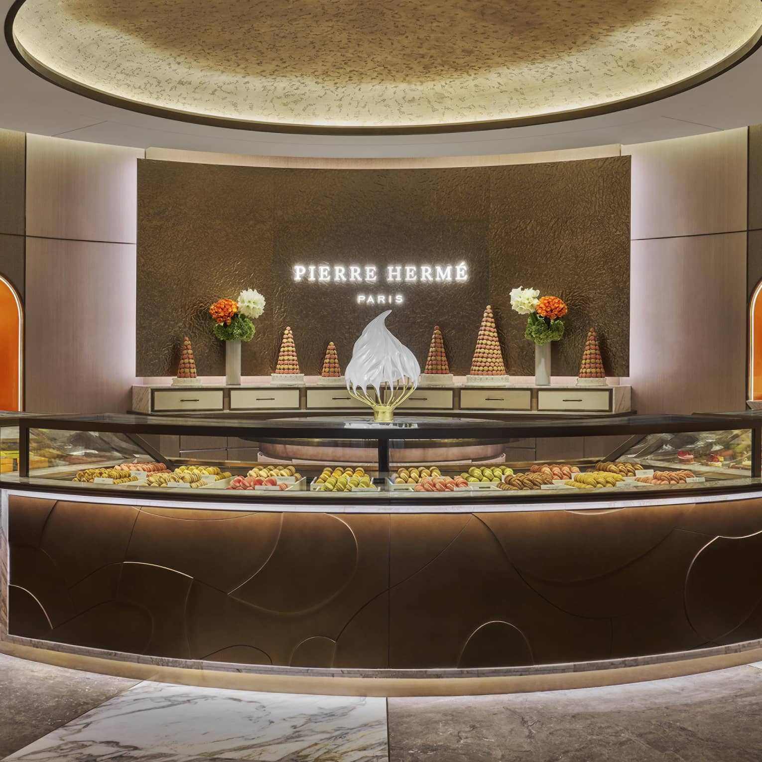 Circular pastry counter with the name Pierre Herm� light up on the wall behind it