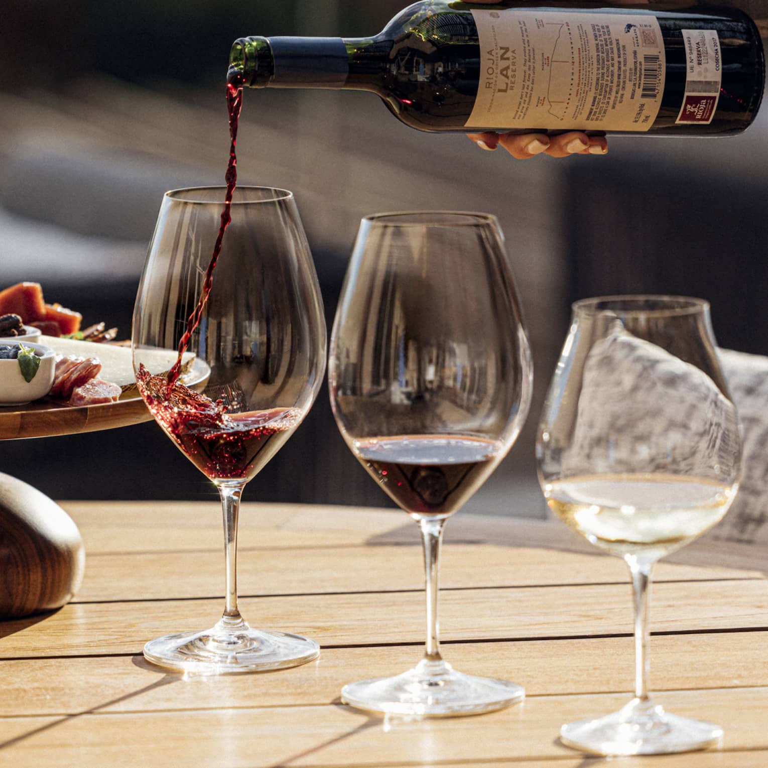 Three glasses of wine are poured next to a plate of charcuterie