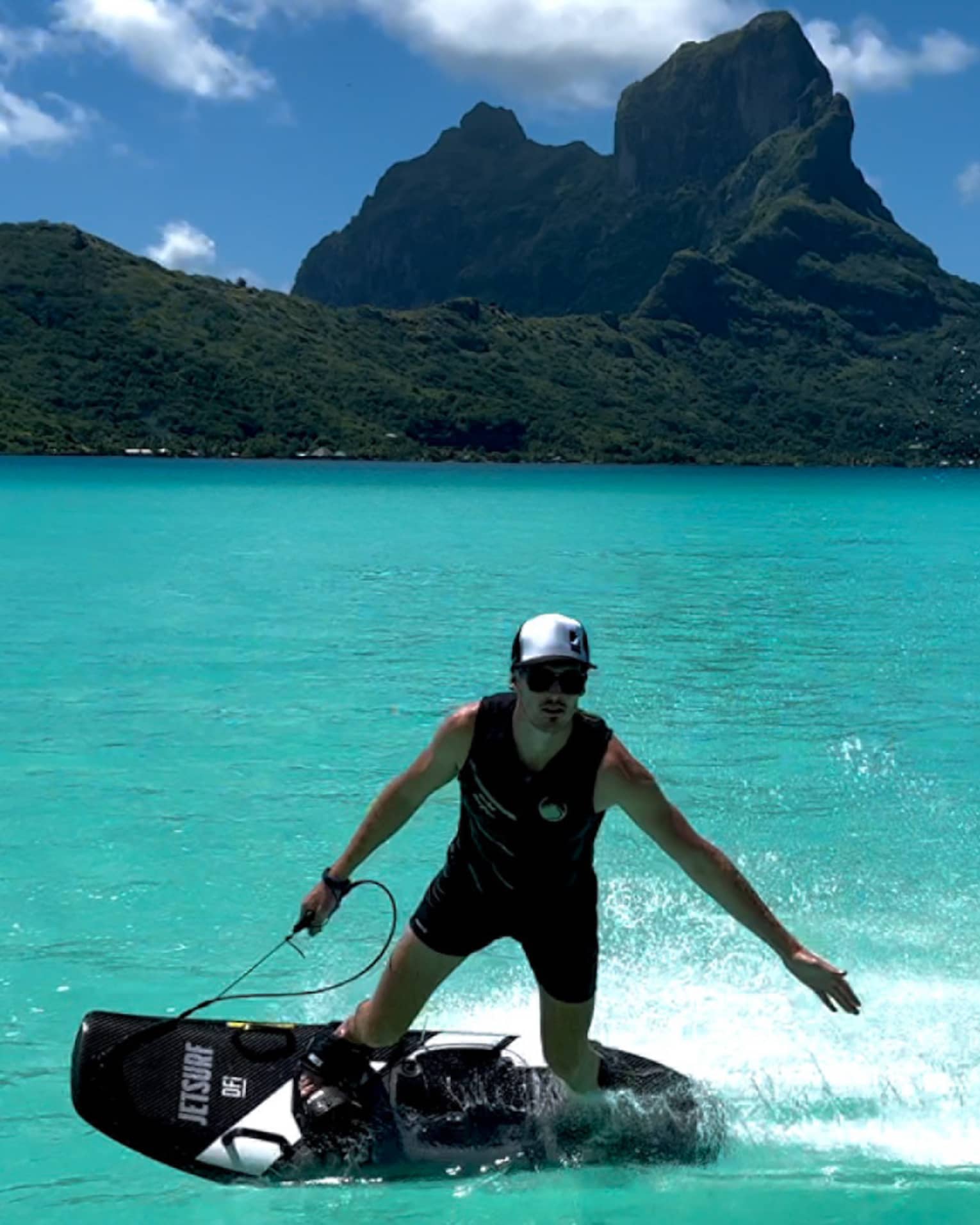Person on JETSURF board rides on turquoise water, mountain visible in background