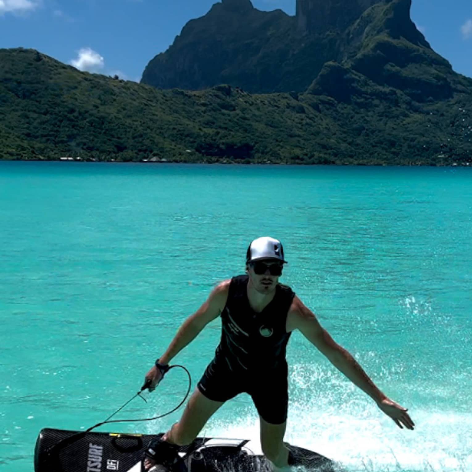 Person on JETSURF board rides on turquoise water, mountain visible in background
