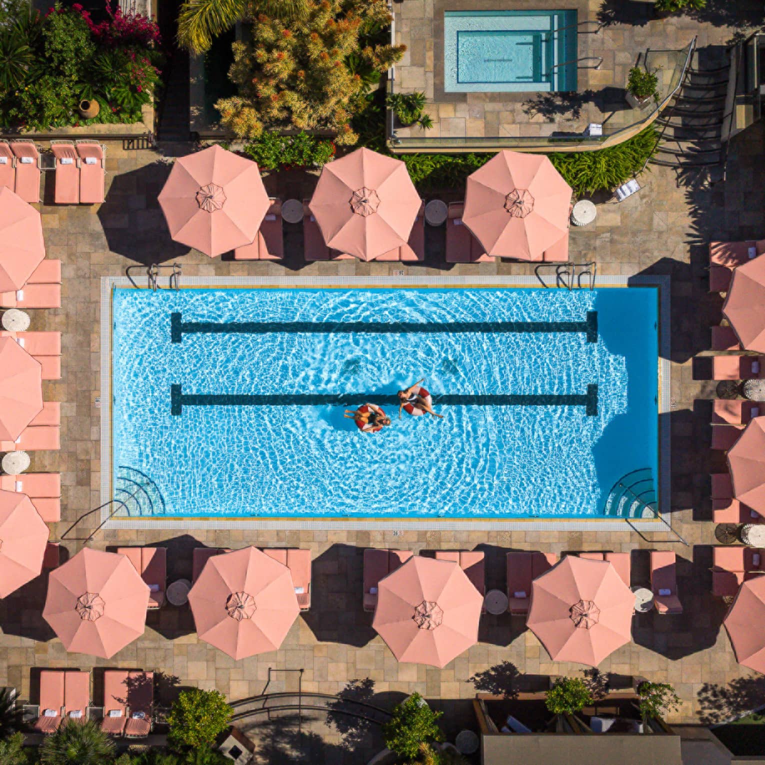 Aerial view of luxury hotel pool surrounded by pink umbrellas and lounge chairs