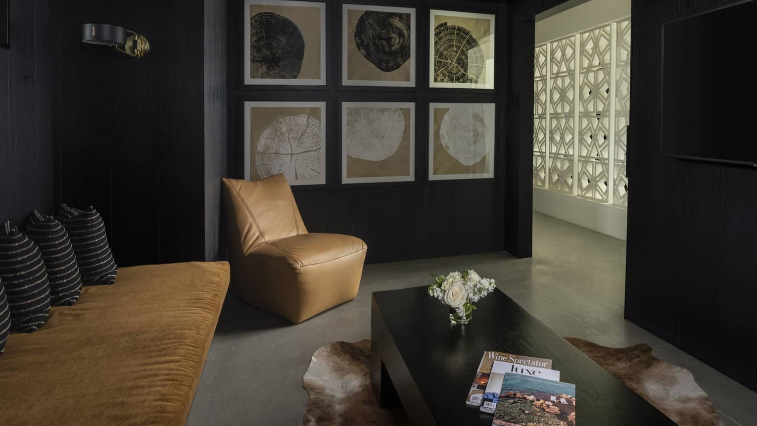 Luxury villa lounge area with black walls, sofa, camel leather chair, low black coffee table, wall-mounted TV and six pieces of framed wall artwork