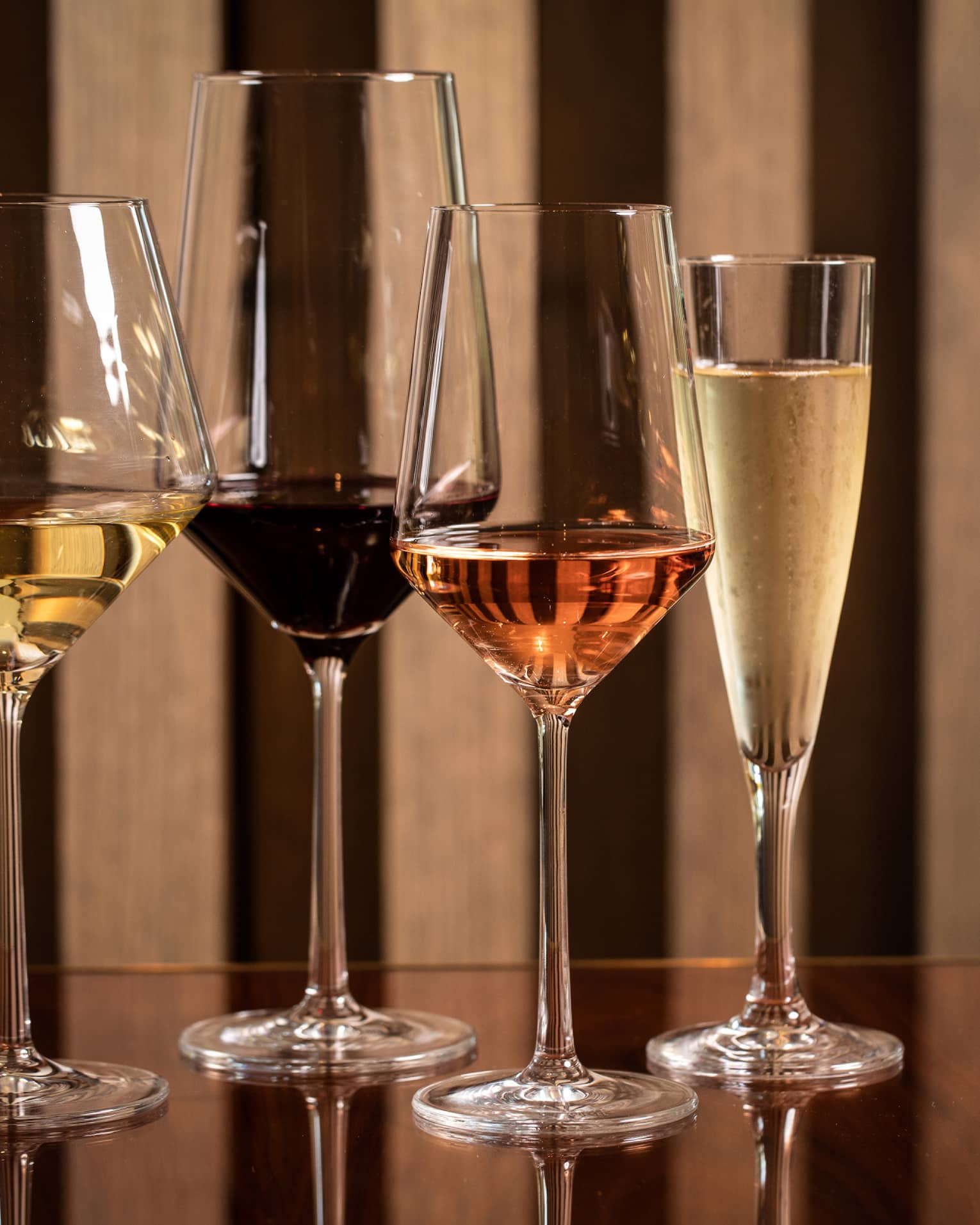 Four modern wine glasses holding white, red and rose wine are lined up on a wooden table 