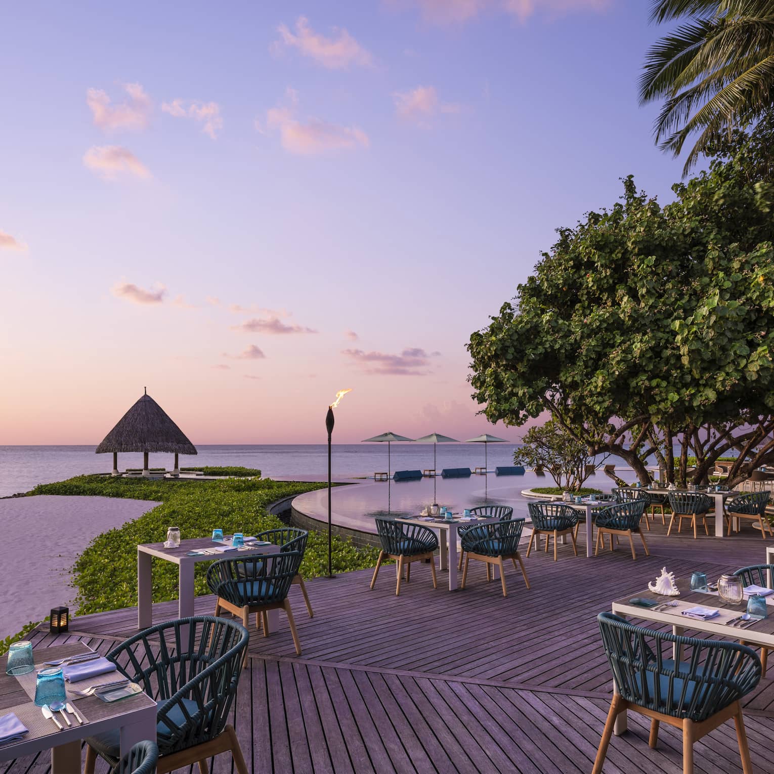 Tiki torches line the oceanside Reef Club terrace that's ready for guests with tables set with plates, silverware, blue napkins, all overlooking the ocean