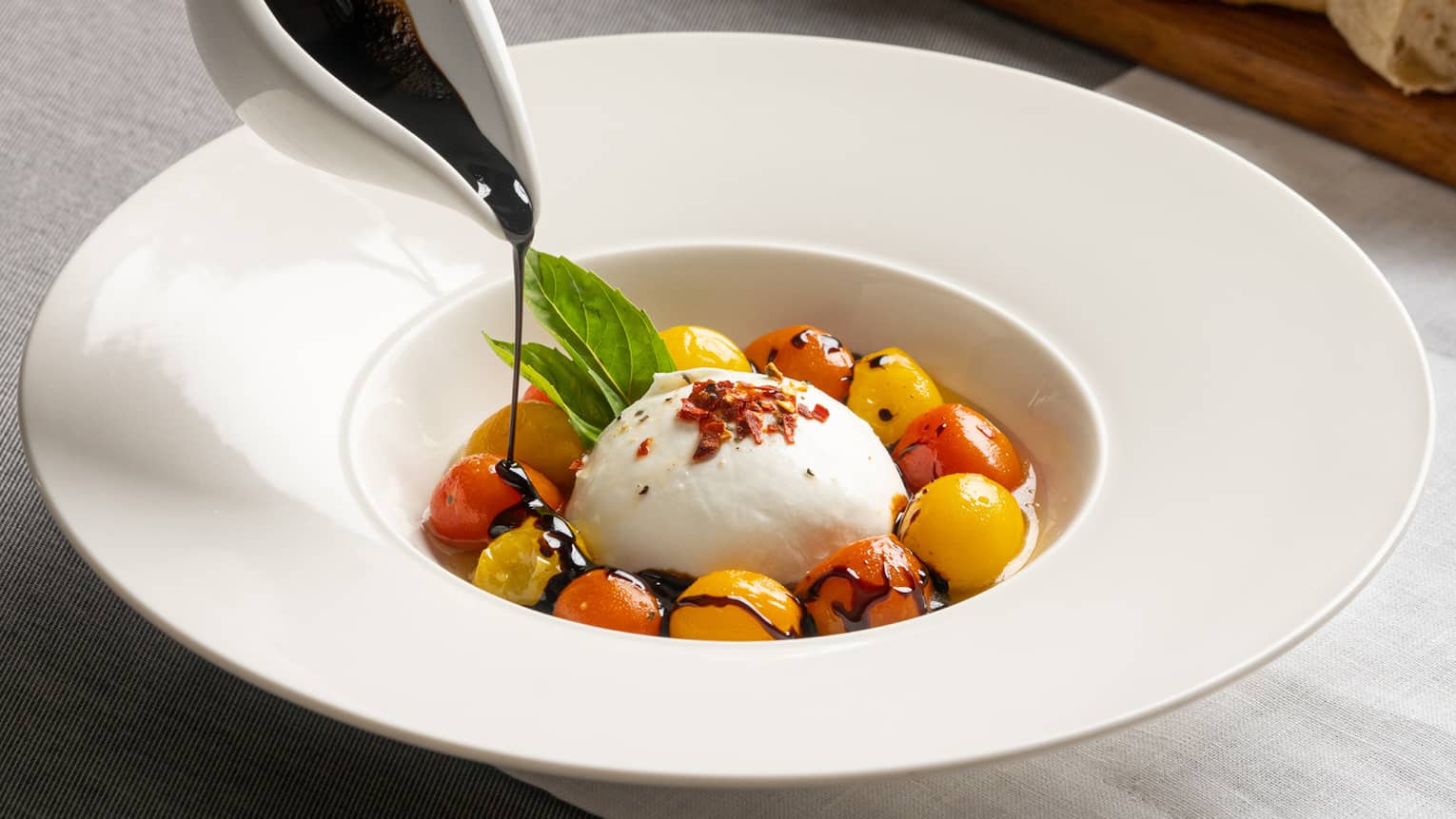 Burrata encircled with red and yellow cherry tomatoes in a white, large-rimmed bowl