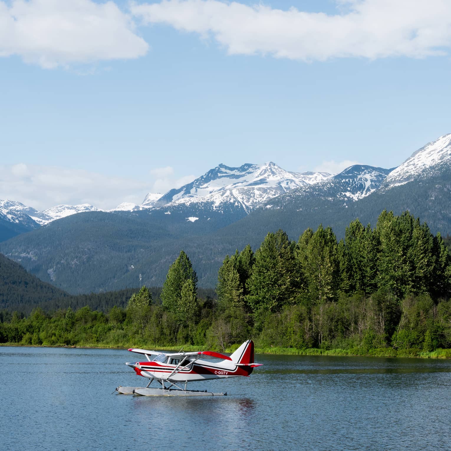 A small plane on a lake surrounded by forest with mountains in the background.