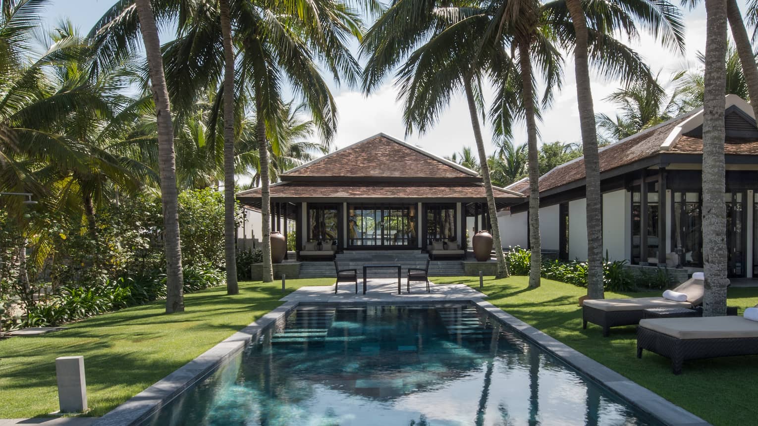 Pool villa, small patio table at end of outdoor swimming pool under palms