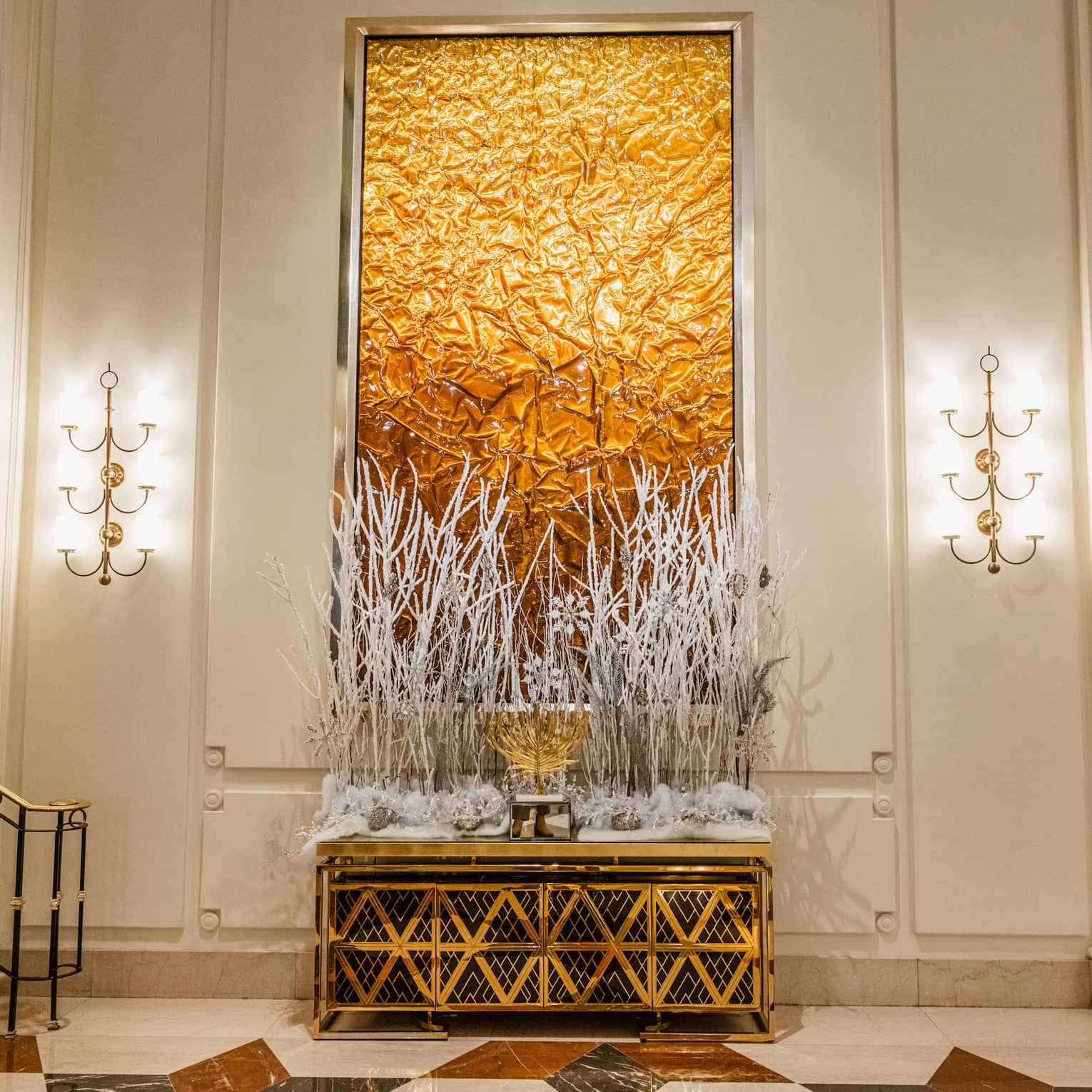 Gold menorah is set on a gold table decorated with white branches and snow-covered greenery in a hotel lobby