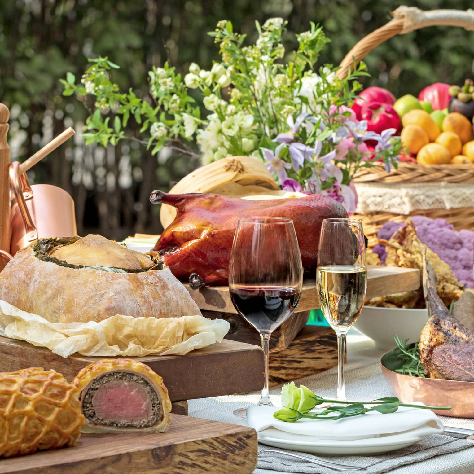 Close-up of food table with wine, basket with fruit, platters with roasted meats, fried duck, bread