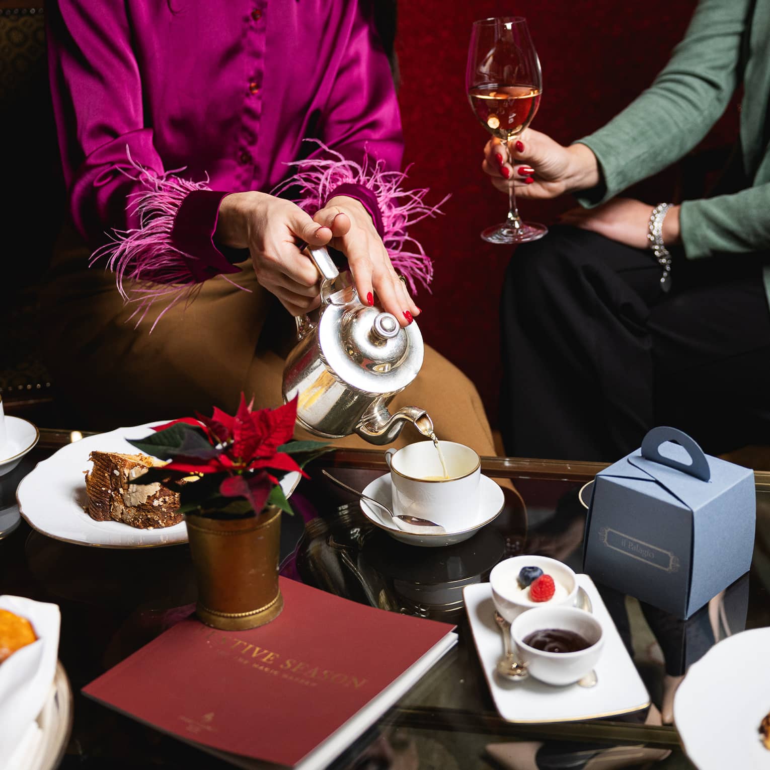 Two people enjoying afternoon tea with wine at a coffee table set with festive foods