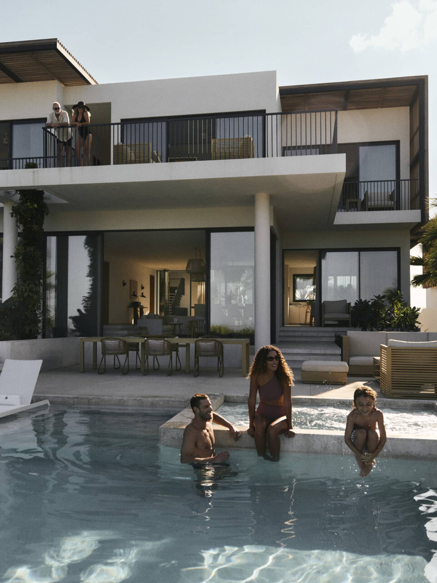 A woman, man and young child sit on edge of private pool at luxury residence in tropical setting
