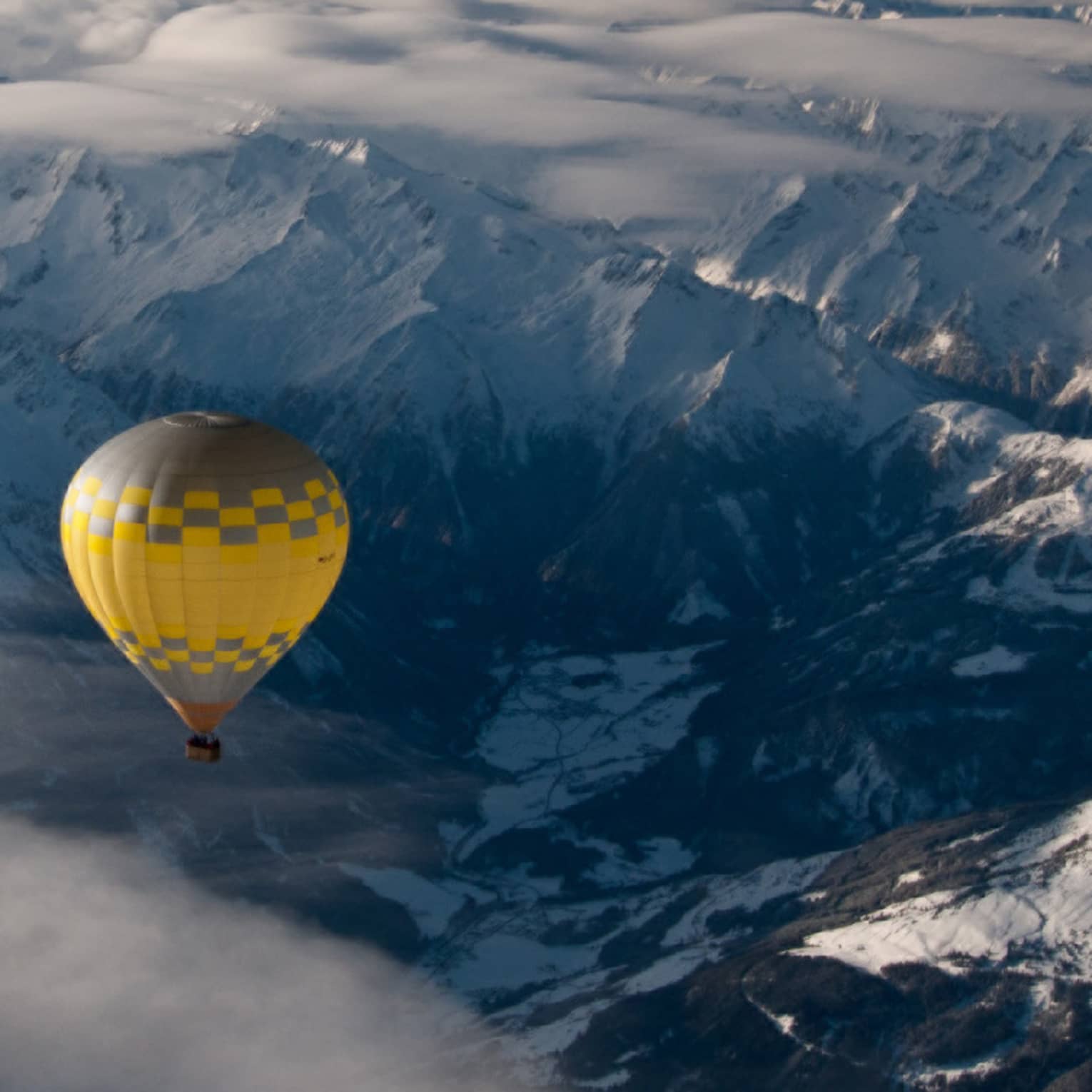 Yellow hot air balloon soaring over the snow-covered Alps