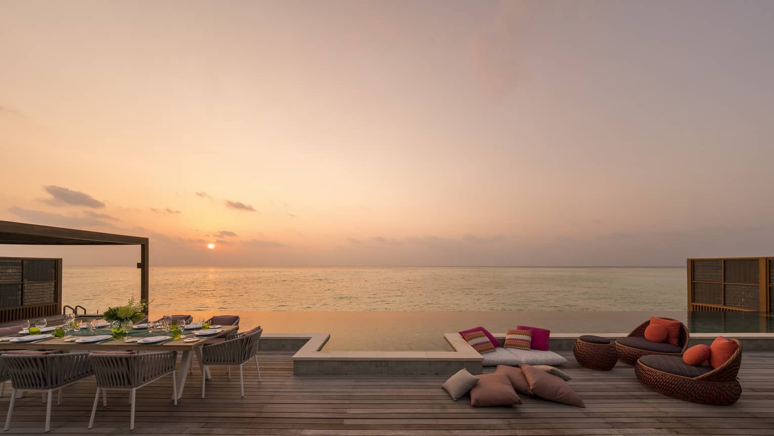 Outdoor deck with a dining table, lounge seating and an infinity pool overlooking the ocean at sunset