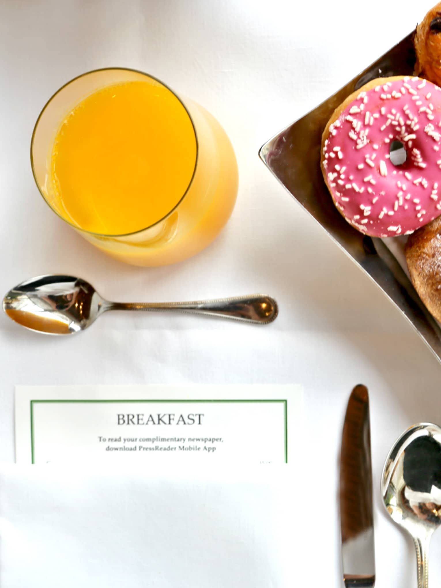 Aerial view of in-room breakfast table with menu, tray with pastries, doughnut with pink icing, orange juice