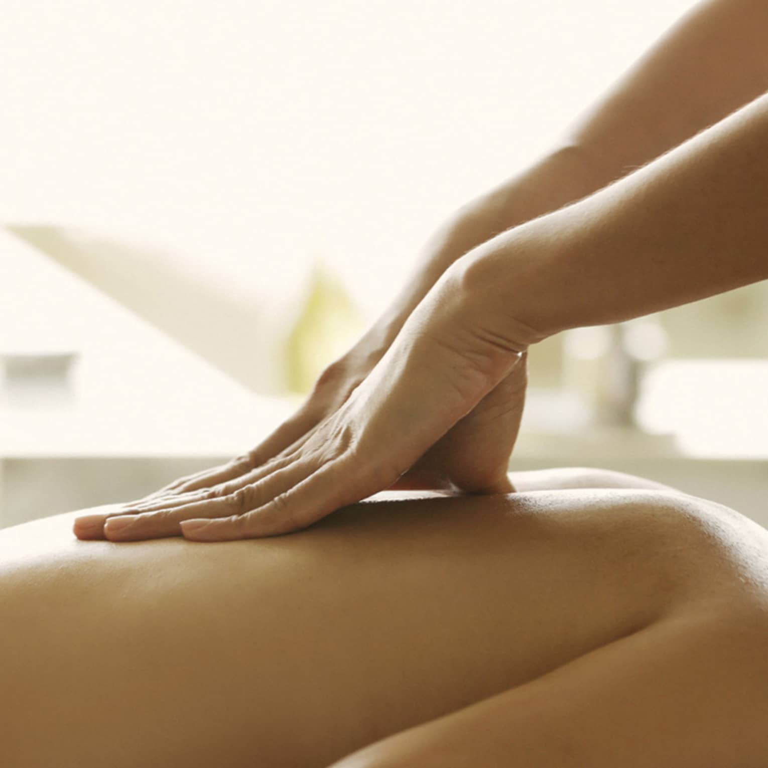 Masseuse reaches over, massages woman's bare back as she lies on spa table