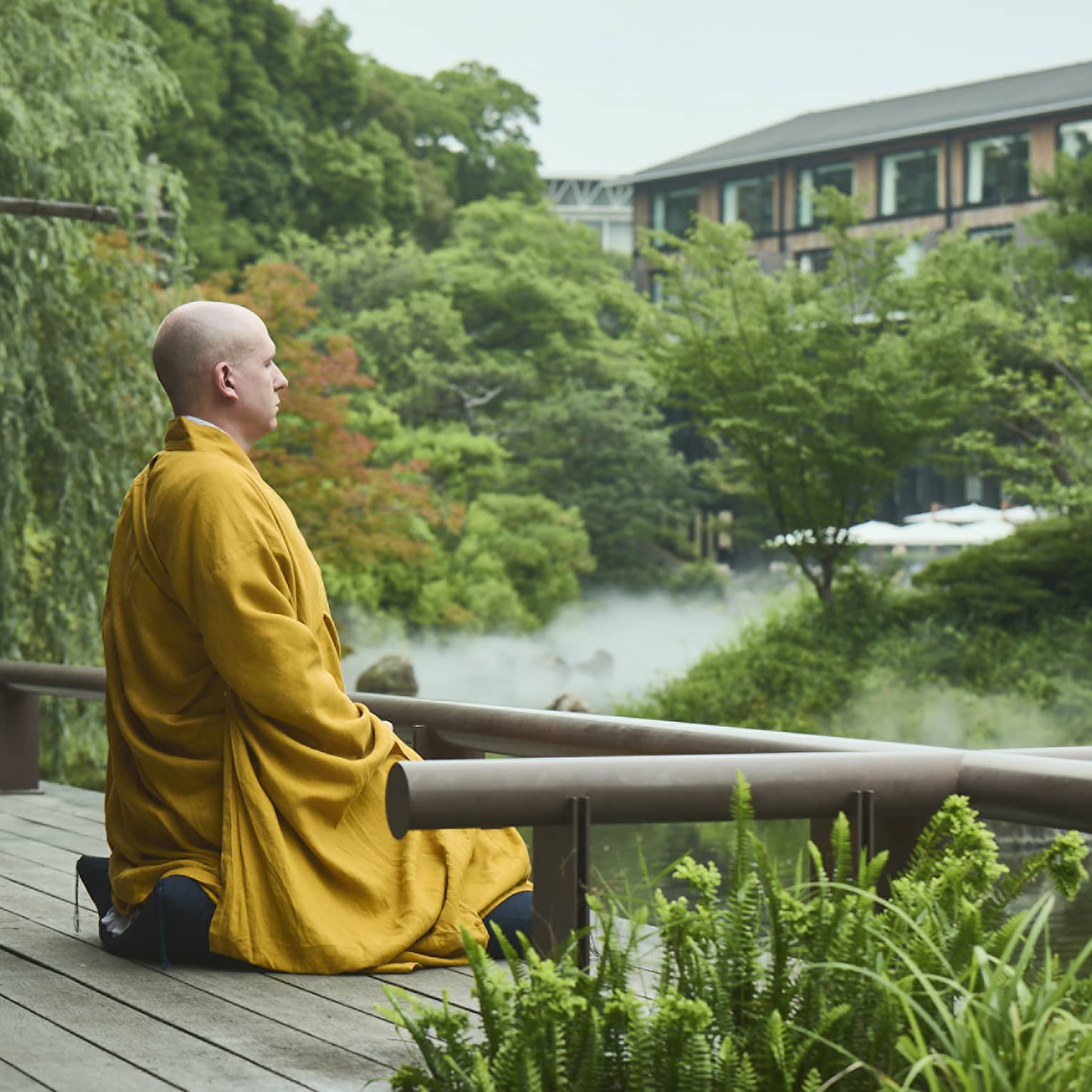 A monk sits at the edge of a serene pond