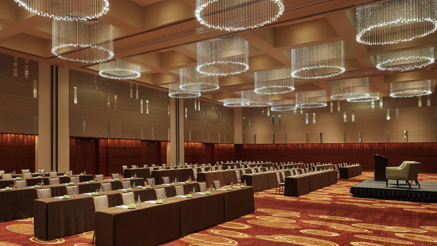 Intricate hanging lights hang above rows of tables and chairs facing the front of the room