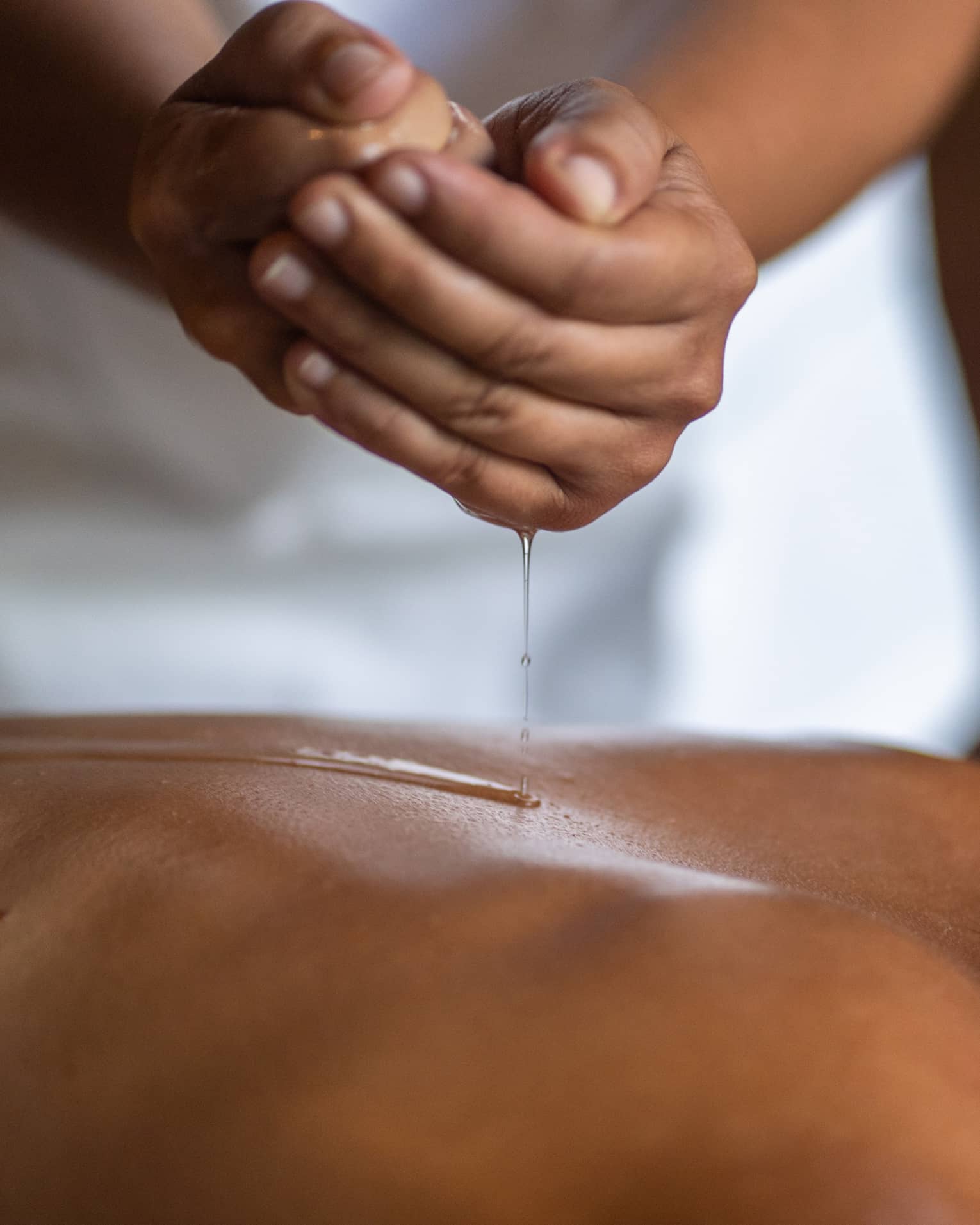 Delicate hands apply oil to a guest's back during a spa treatment