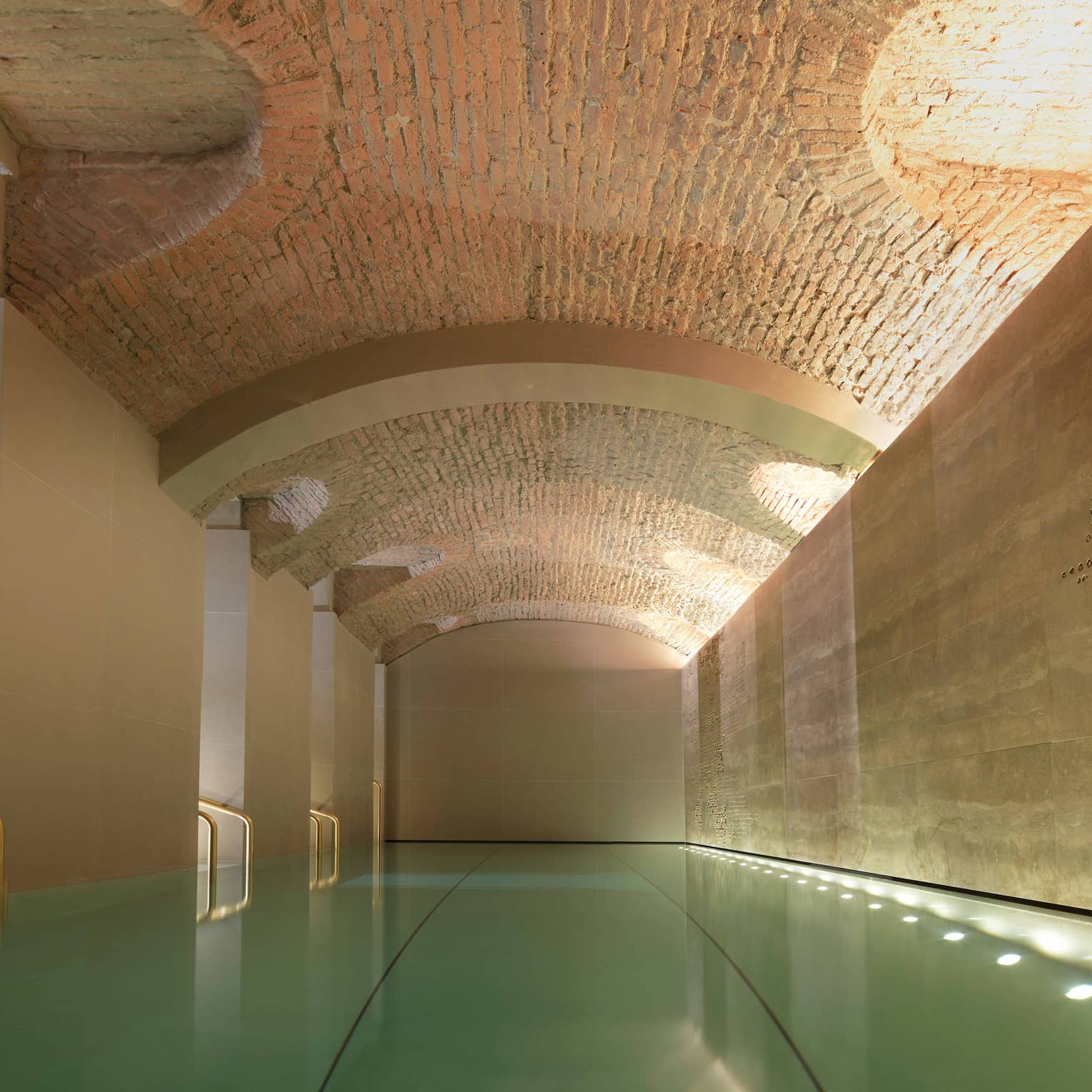 Indoor lap swimming pool with gold railings under curved stone ceiling