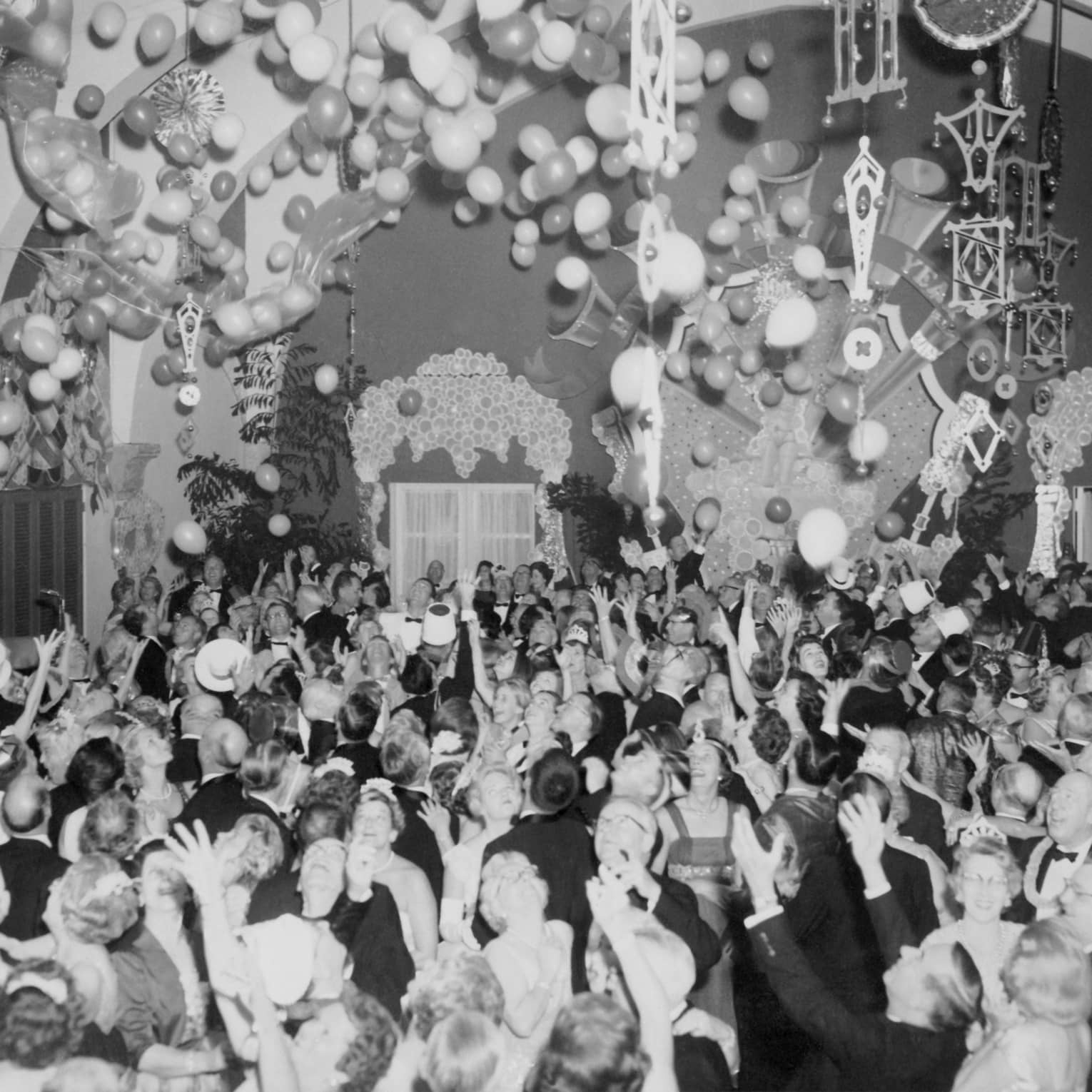 A black and white photo of a large group of people celebrating with balloons in a large room.