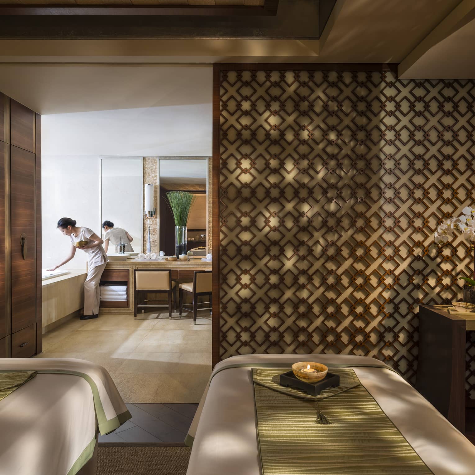 Couples massage beds side-by-side in spa room with candles and staff preparing bath