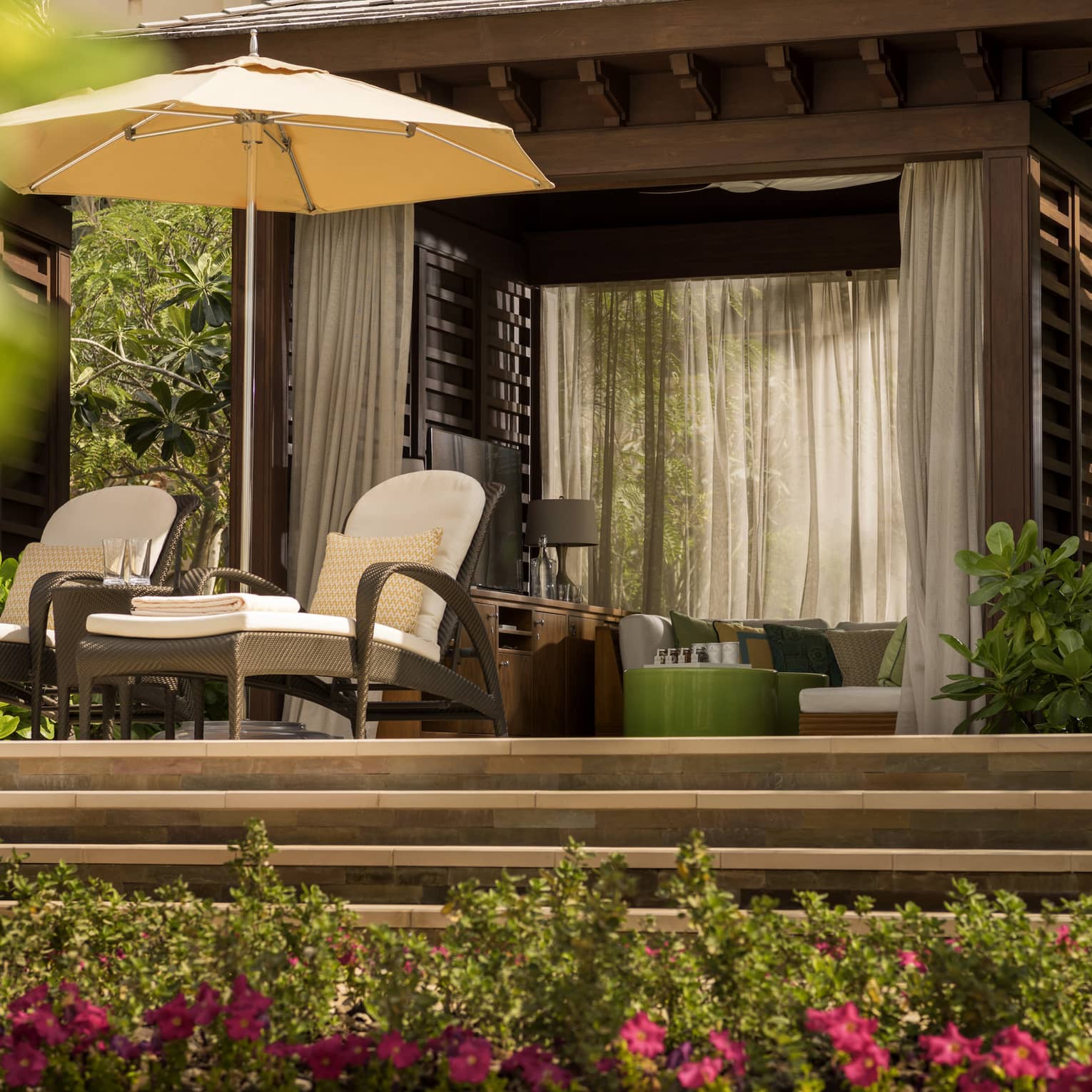 Two wicker chairs on a patio above several flowery bushes.
