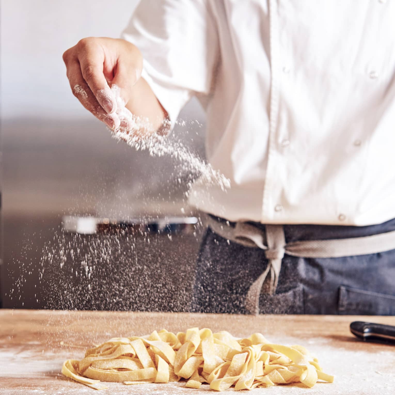 Noe chef sprinkles white flour over thick fresh pasta noodles on counter
