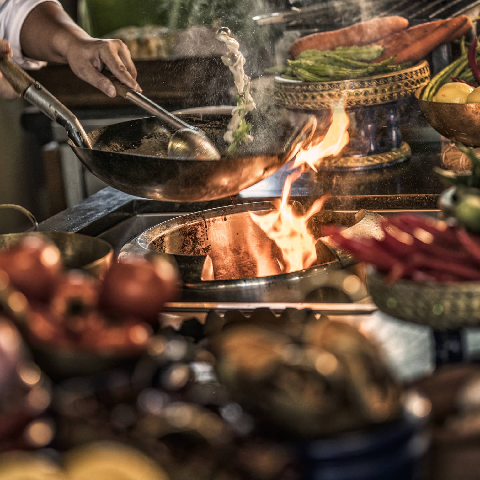 Close-up of chef stirring meals in copper pans over stove, flames 