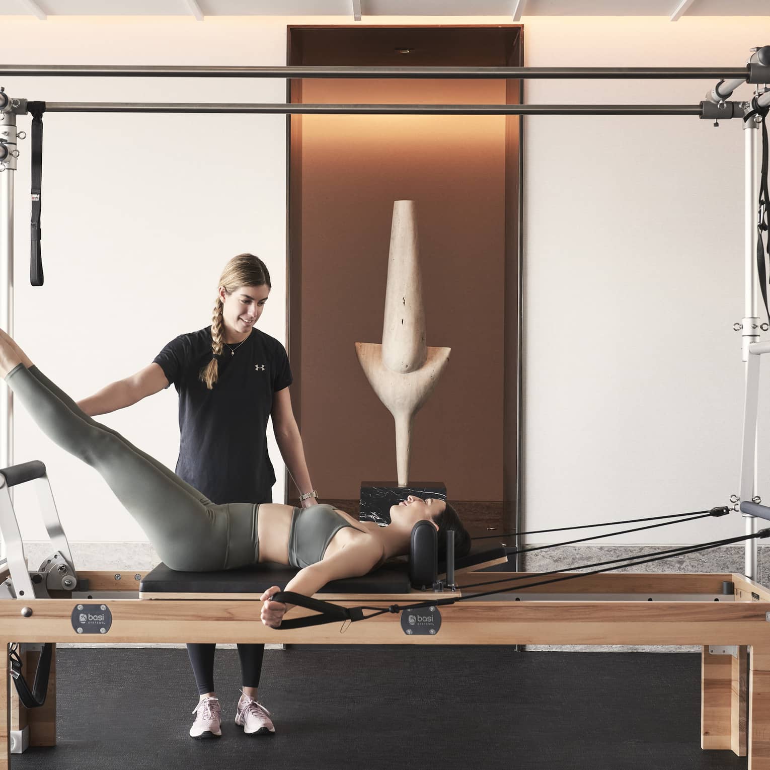 Fitness coach holds legs of woman lying and working out on a Pilates reformer