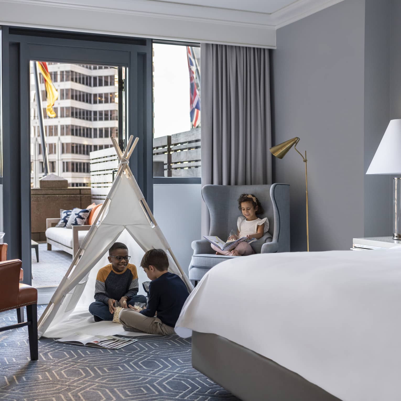 Children sitting in a tent and on a chair in a hotel room.