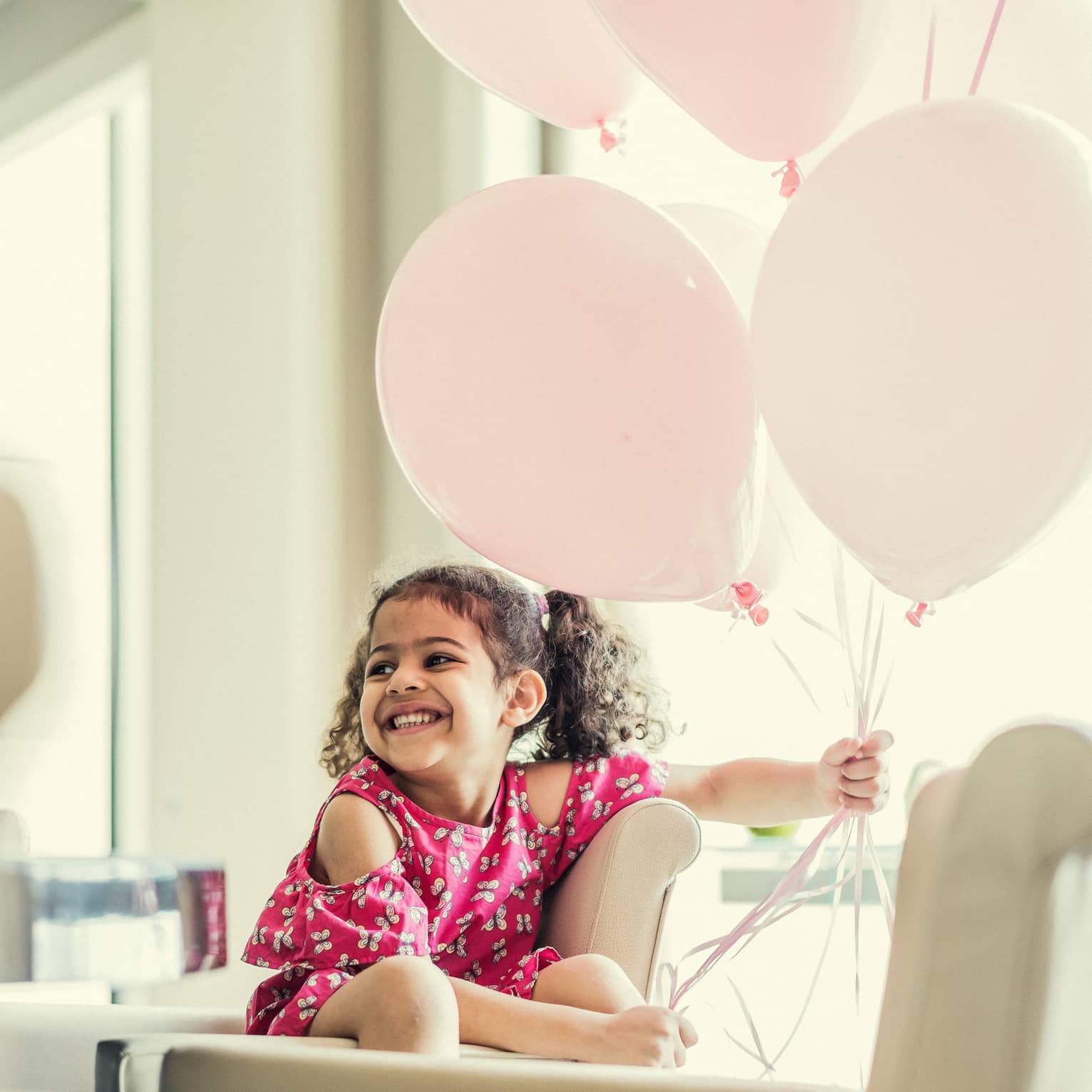 Child smiling whilst holding pink balloons