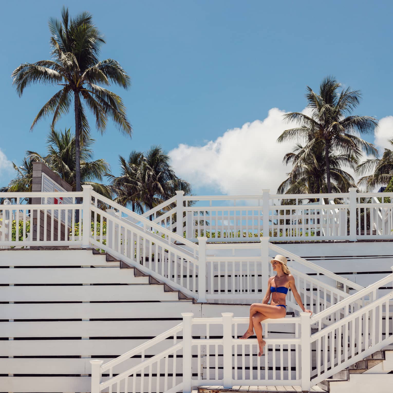 A person wearing a swimsuit and sitting on a staircase leading to the shore