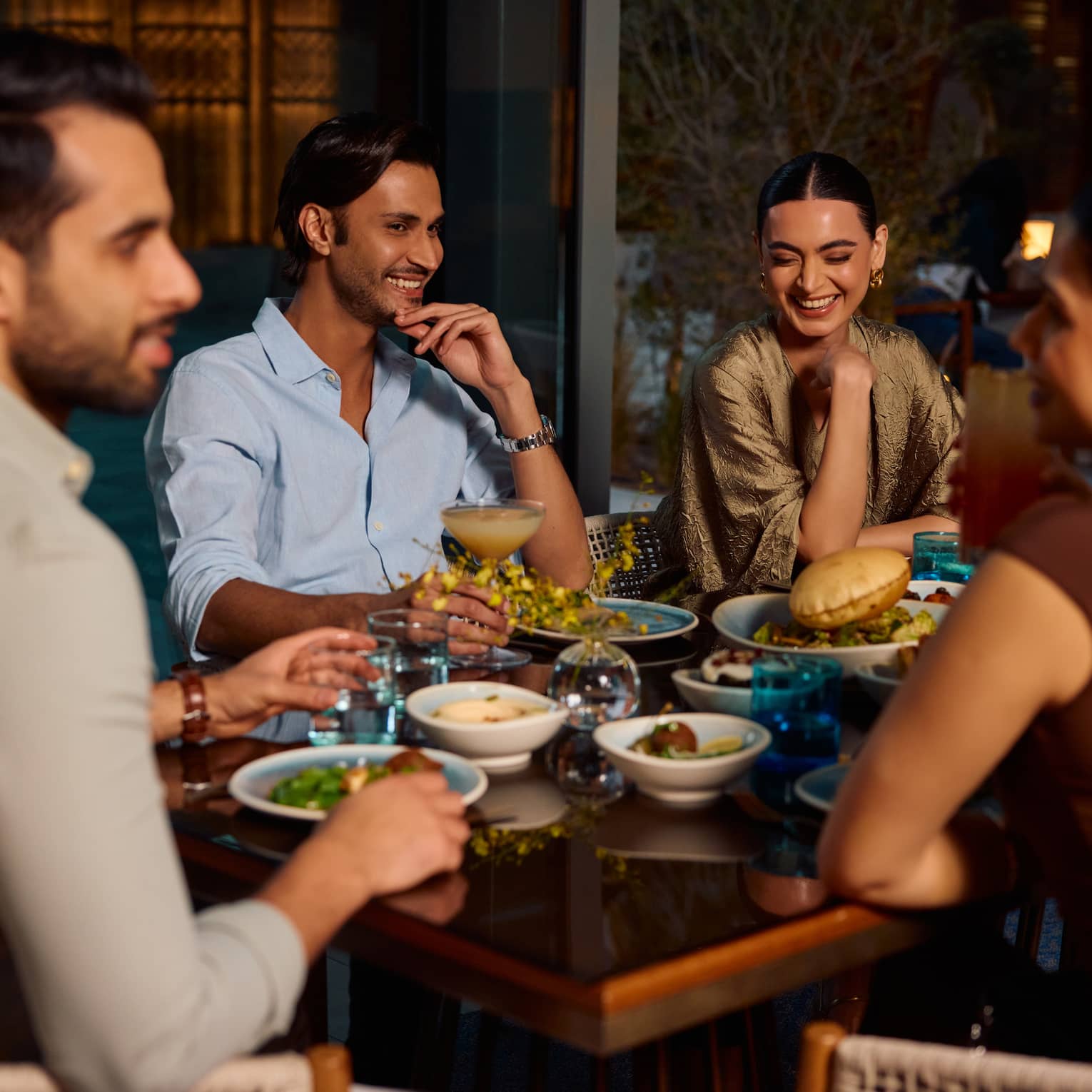 A group of four people sit smiling around a restaurant table filled with food
