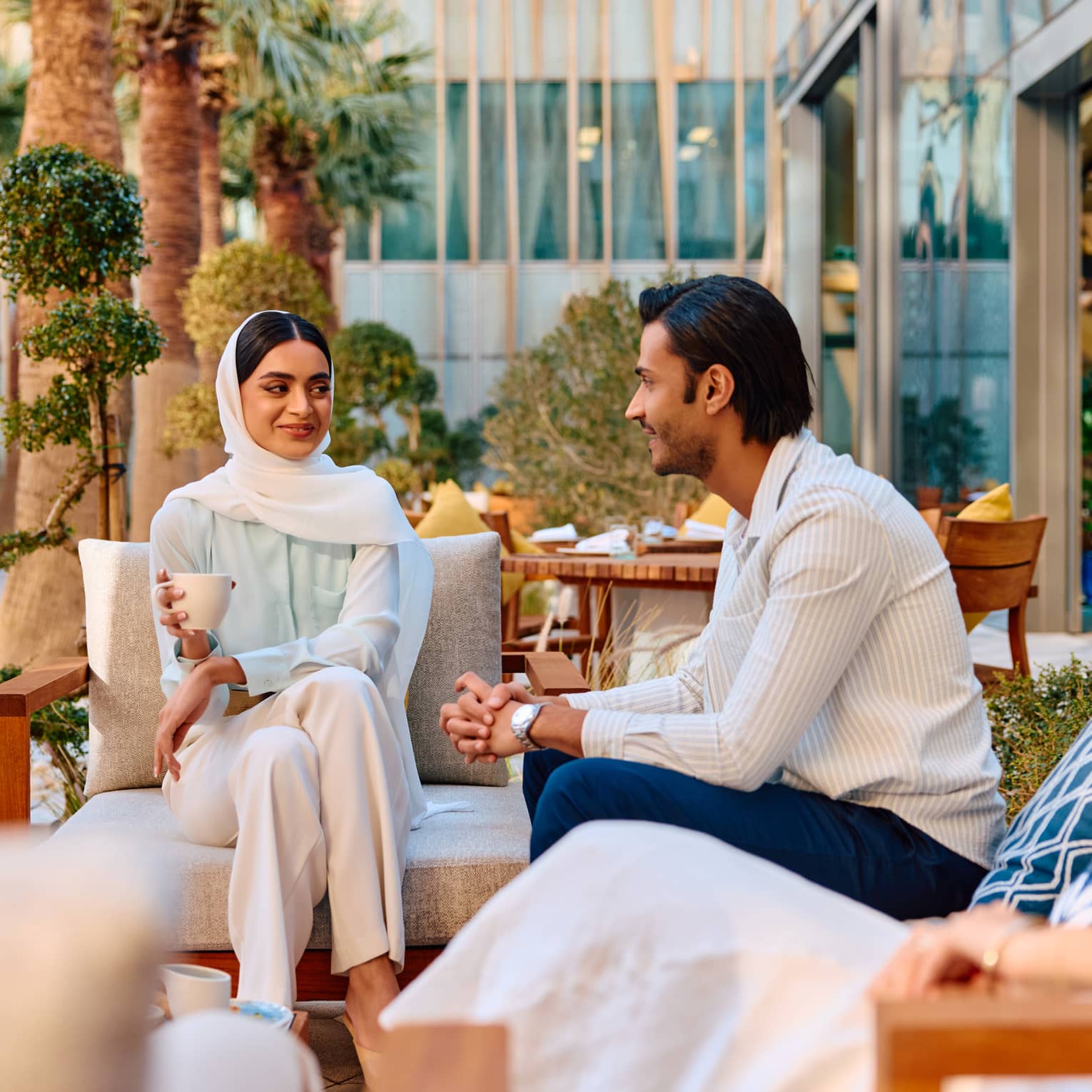 A couple sits in an outdoor lounge seating are smiling at each other