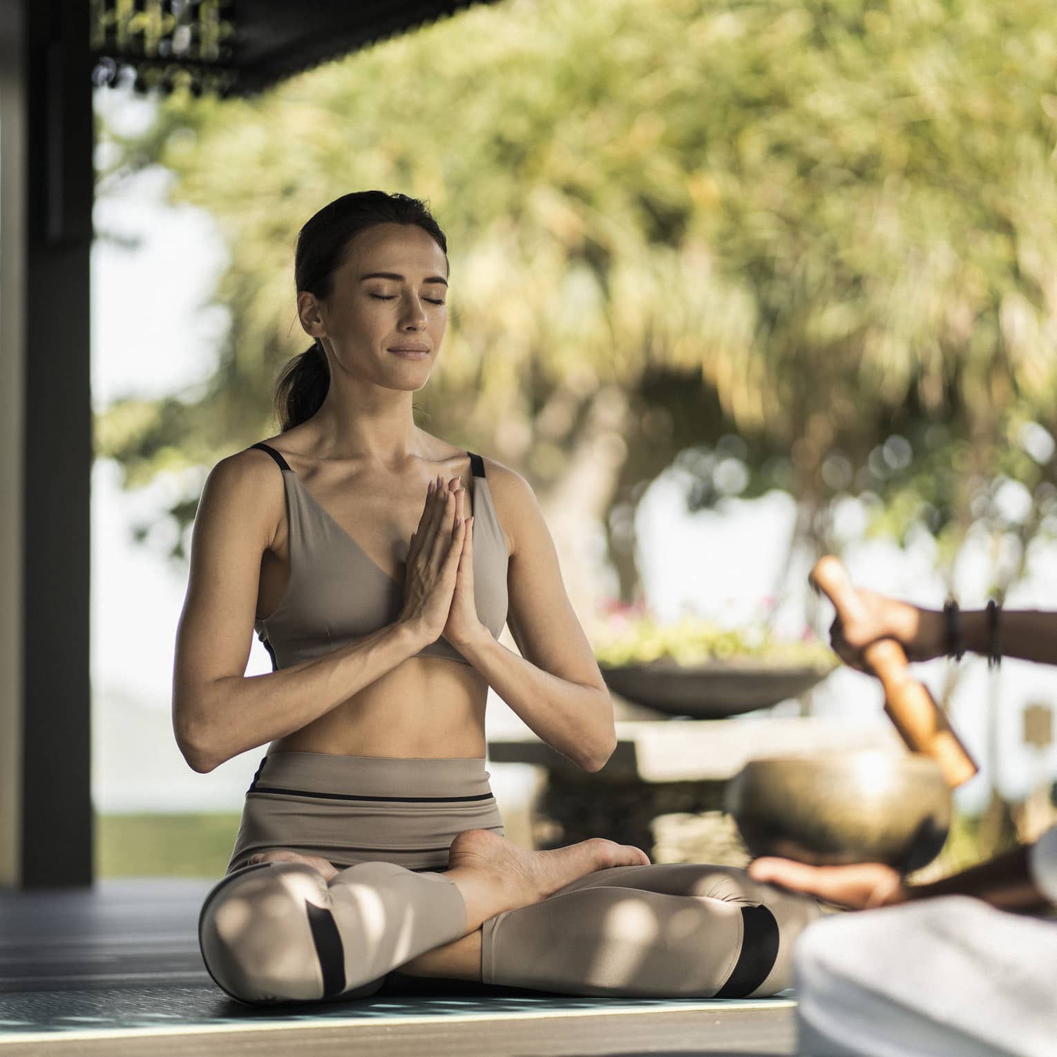 A woman sitting outside doing a yoga breathing pose.