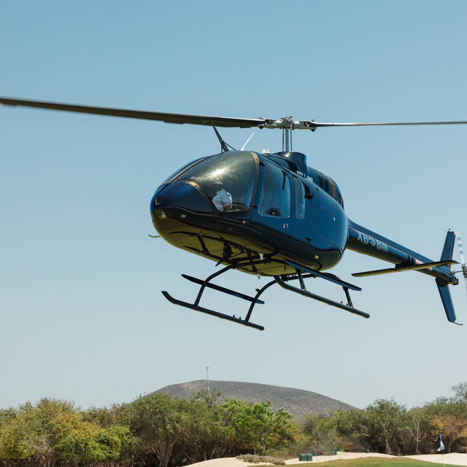 Black helicopter rising just above a tree line with a clear blue sky in the background